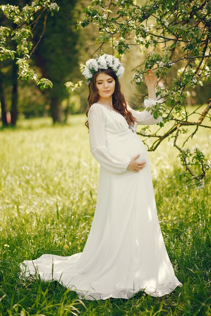 그녀의 머리에 길고 흰 드레스와 화환에 아름 다운 젊은 임신 한 여자