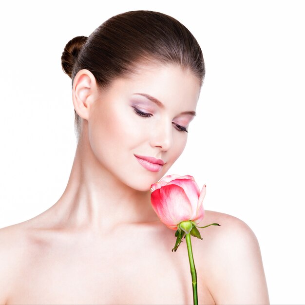 Beautiful young pretty woman with healthy skin and pink rose near face - isolated on white.