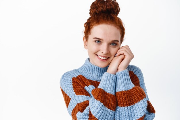 Beautiful young redhead woman with pale skin and blue eyes, smiling natural and touching face with clasped hands, gazing with romantic expression on white