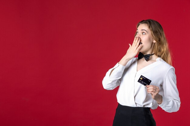 beautiful young shocked female server butterfly on the neck and holding bank card on red background