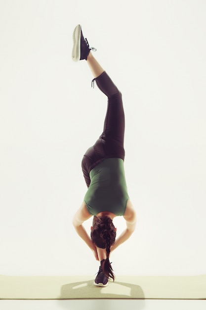 Beautiful young slim woman doing stretching exercises at the gym against white