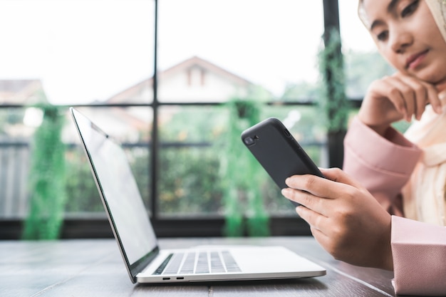 Foto gratuita bella giovane donna musulmana asiatica sorridente che lavora al telefono che si siede nel salone a casa