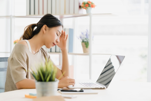 Free photo beautiful young smiling asian woman working laptop on desk in living room at home