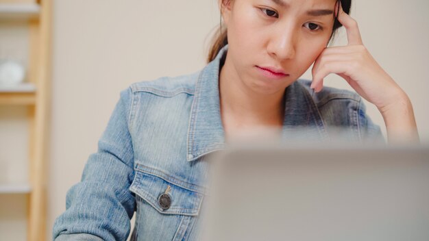無料写真 美しい若い笑顔アジア女性自宅のリビングルームの机の上のノートパソコンで作業します。アジアビジネスの女性がホームオフィスでノートブック書類ファイナンスと電卓を書きます。