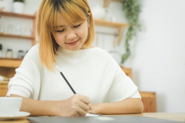 Beautiful young smiling asian woman working on laptop while sitting in a living room at home