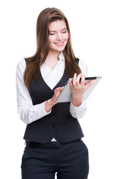 Красивая молодая усмехаясь бизнес-леди в сером костюме с помощью планшета на белом фоне.