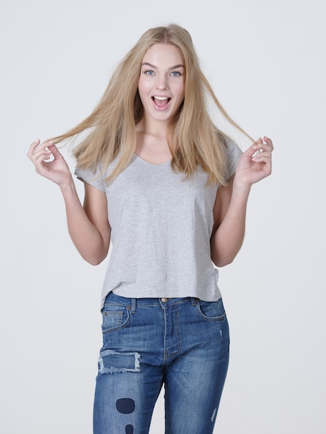 Bella giovane donna caucasica sorridente con capelli biondi lunghi che posano su priorità bassa bianca.