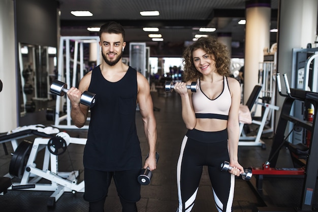 Beautiful young sporty couple showing muscle and workout in gym during training
