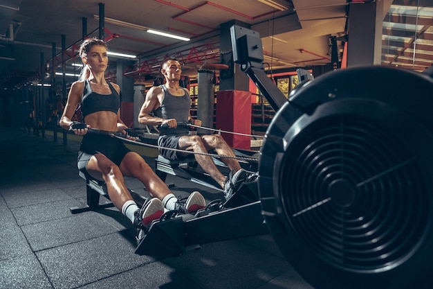 Beautiful young sporty couple workout in gym together. Caucasian man training with female trainer.