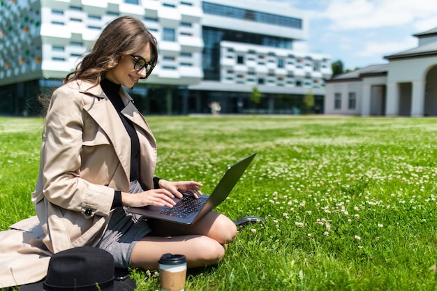 Beautiful young student using laptop on grass in campus