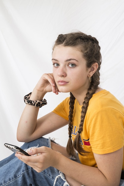 Beautiful young teenager in a yellow shirt and ripped jeans with braided hair texting on the phone