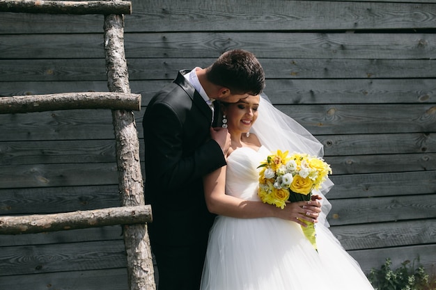 Beautiful young wedding couple stands near the old wooden house