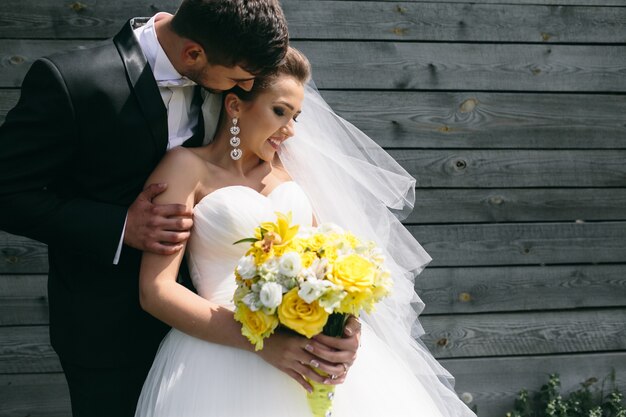 Beautiful young wedding couple stands near the old wooden house