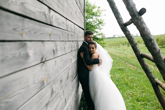 美しい若い結婚式のカップルが古い木造住宅の近くに立っています