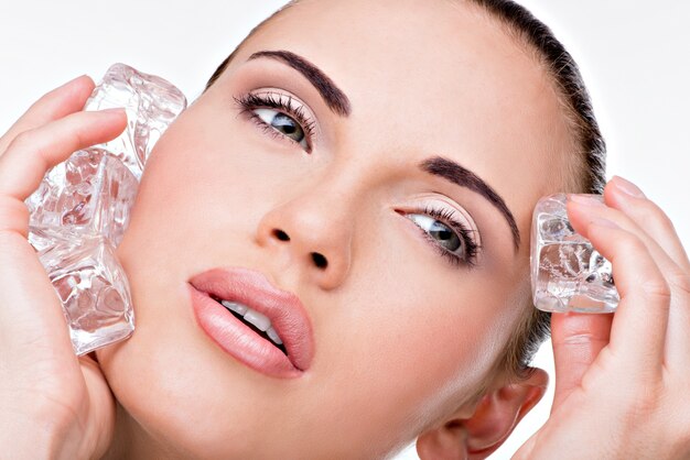 Beautiful young woman applies the ice to face. Skin care concept.