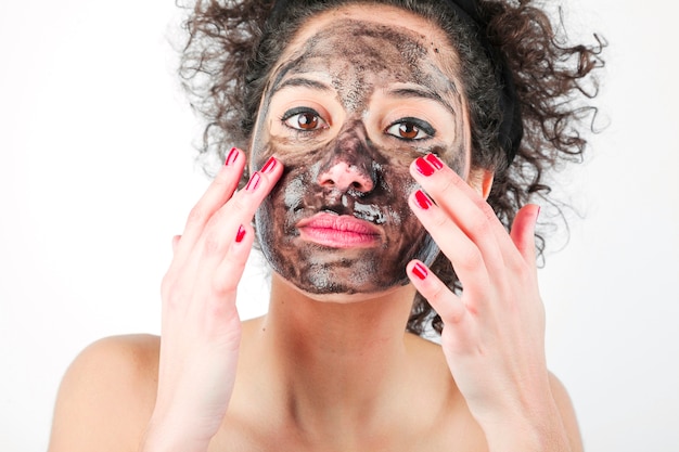 Foto gratuita bella giovane donna che applica la maschera di protezione nera con le sue dita contro fondo bianco