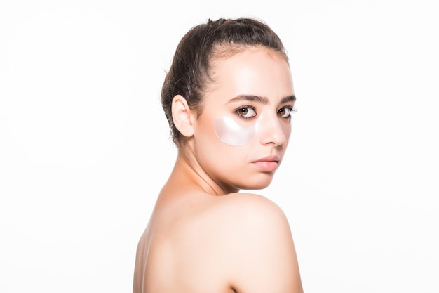 Beautiful young woman applying cosmetic under eyes isolated on white wall