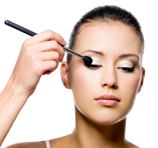 Beautiful young woman applying eyeshadow with brush on white background