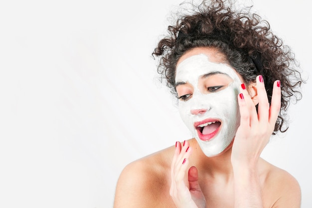 Beautiful young woman applying facial mask on her face isolated over white background