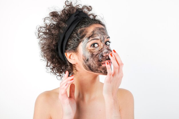 Beautiful young woman applying facial mask on her face over white background