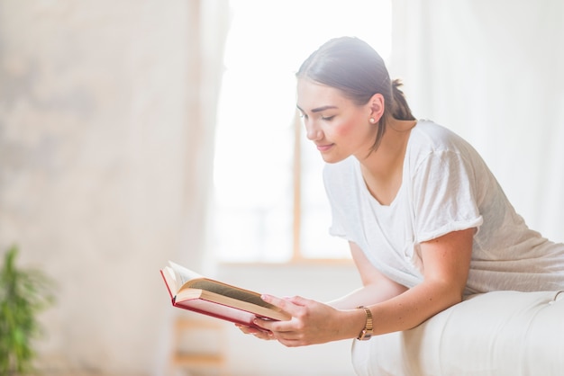 Beautiful young woman on bed reading book