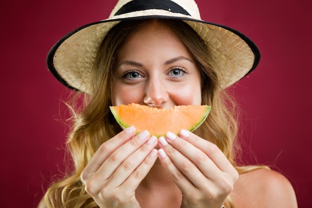 Beautiful young woman in bikini eating melon. Isolated on red.