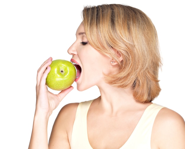 Beautiful young woman biting the biting a fresh ripe apple on white.