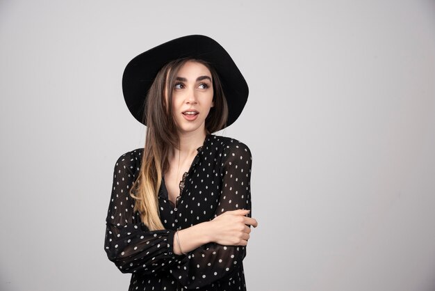 Beautiful young woman in black hat standing arms crossed.