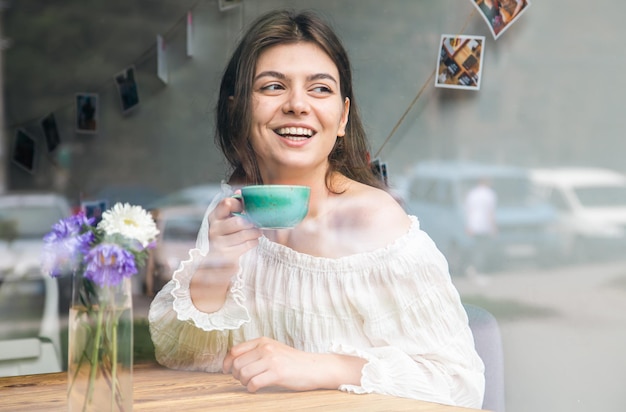 一杯のコーヒーが通りから見えるカフェで美しい若い女性