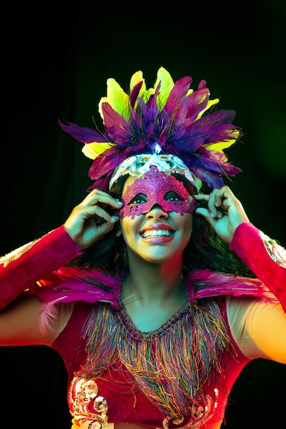 カラフルな光のカーニバルマスクと仮面舞踏会の衣装で美しい若い女性
