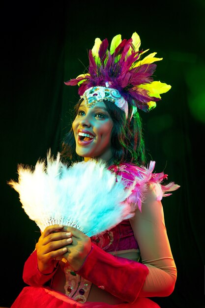 Beautiful young woman in carnival mask and masquerade costume in colorful lights