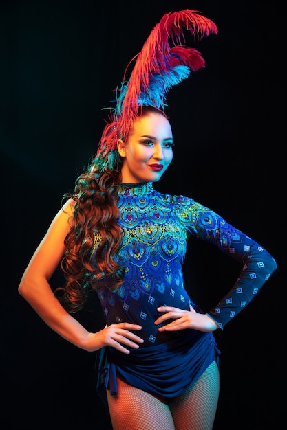 Beautiful young woman in carnival and masquerade costume in colorful neon lights on black