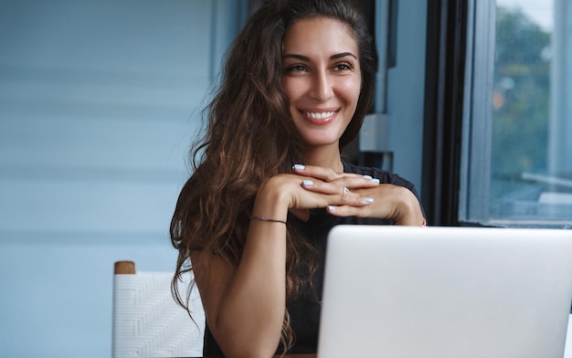 노트북을 사용하고 실내에서 일하는 동안 웃고 있는 캐주얼한 옷을 입은 아름다운 젊은 여성