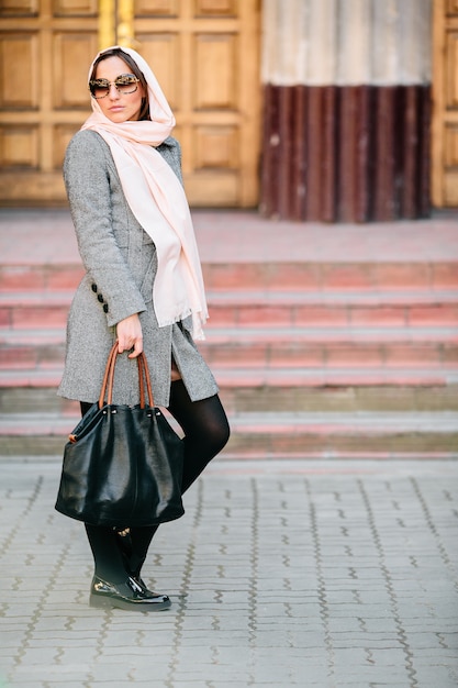 Beautiful young woman in a coat with a bag posing