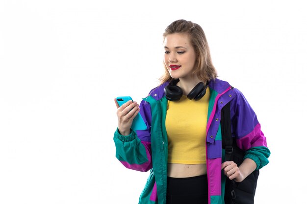 Красивая молодая женщина в красочной куртке и наушниках и с помощью смартфона