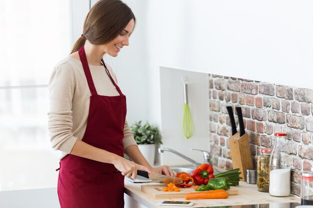 Beautiful young woman cutting fresh vegetables in the kitchen.