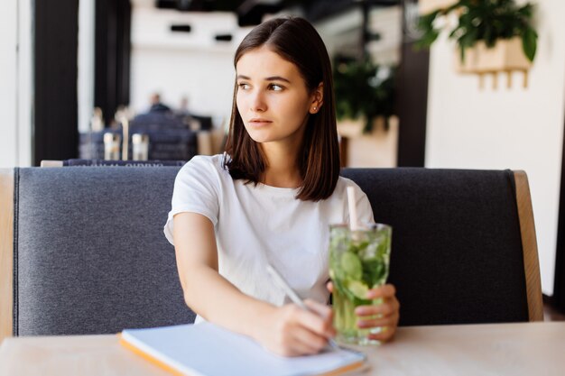 美しい若い女性がカフェでレモネードを飲む