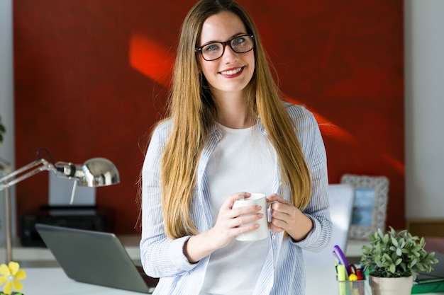 Красивая молодая женщина, пить кофе в офисе.