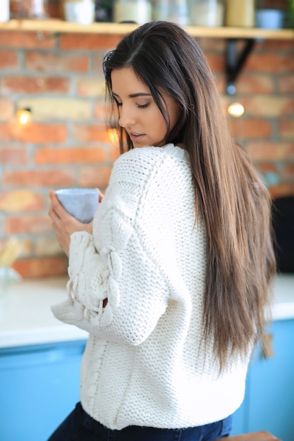 Beautiful young woman drinking coffee or tea in the kitchen