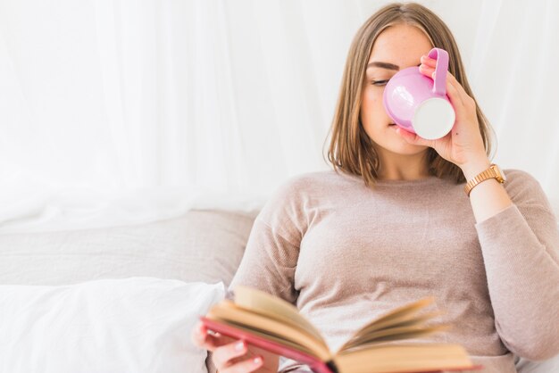 Beautiful young woman drinking coffee while reading book