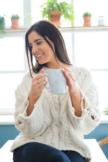 Foto gratuita bella giovane donna che beve una bevanda calda in cucina