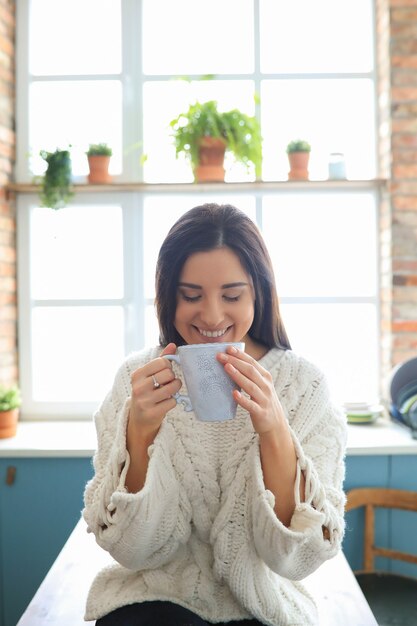 Beautiful young woman drinking a hot drink in the kitchen