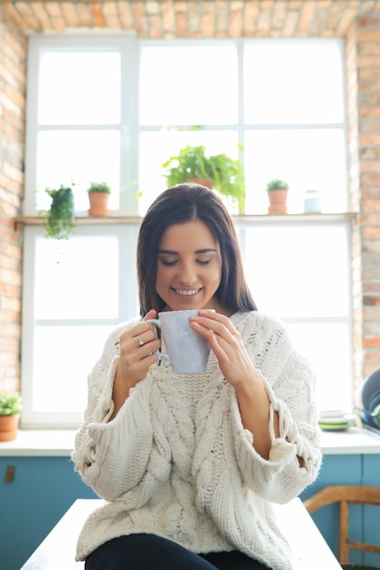 Free photo beautiful young woman drinking a hot drink in the kitchen