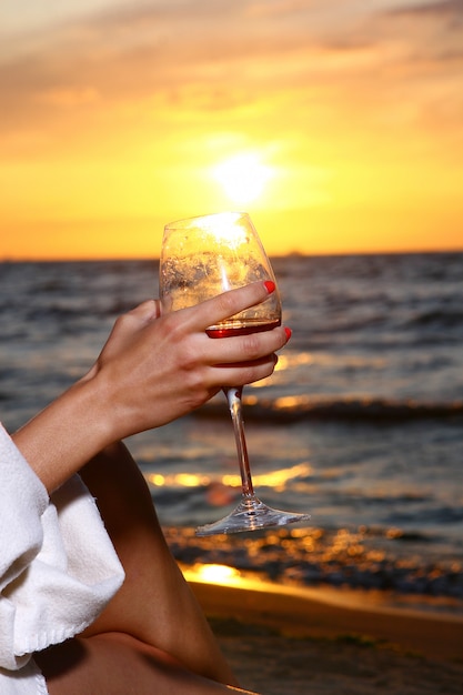 Beautiful young woman drinking wine on beach
