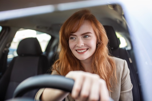 日没時に彼女の新しい車を運転する美しい若い女性車の中で女性車を運転するカジュアルな服装で嬉しいポジティブな表情の女性と気持ちの良い女性の肖像画をクローズアップ