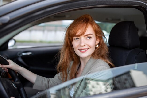 日没時に彼女の新しい車を運転する美しい若い女性車の中で女性車を運転するカジュアルな服装で嬉しいポジティブな表情の女性と気持ちの良い女性の肖像画をクローズアップ