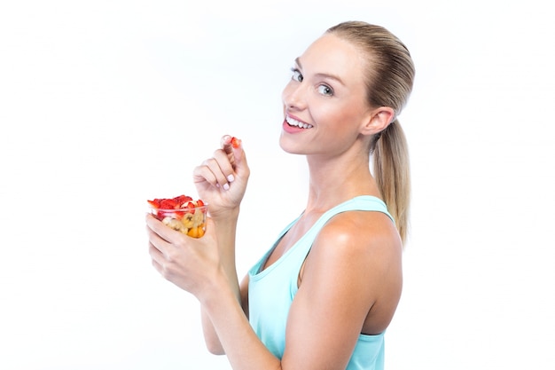 Beautiful young woman eating cereals and fruits over white background.
