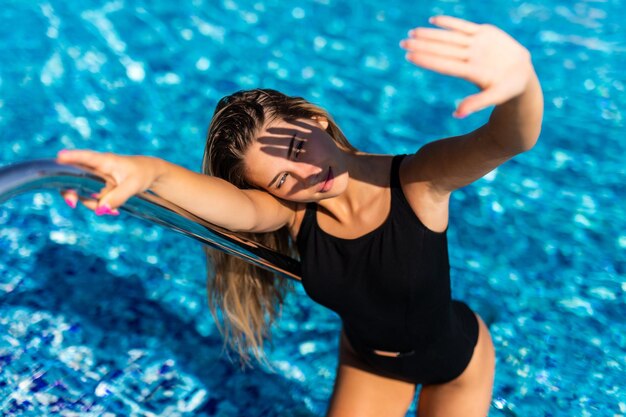 Beautiful young woman entering swimming pool in swimsuit