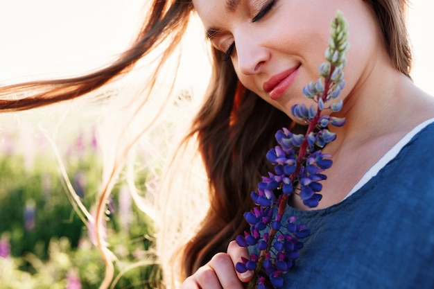 Красивая молодая женщина лицо портрет в люпин поле, проведение цветок возле щек.