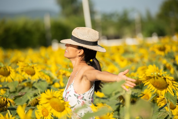 Free photo beautiful young woman in a field of sunflowers in a white dress. travel on the weekend concept. portrait of authentic woman in straw hat . outdoors on the sunflower field.